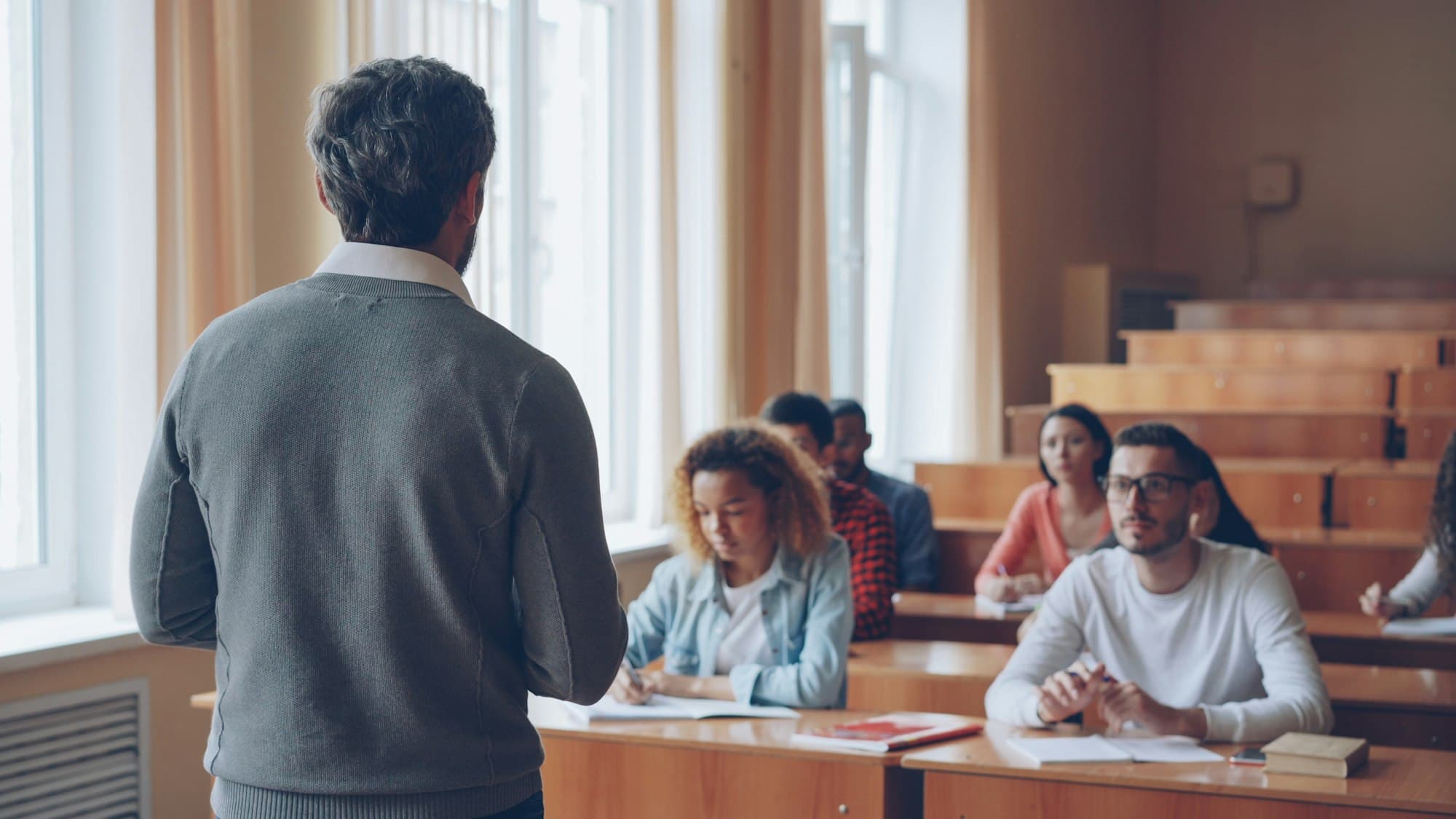 An instructor seen from behind, talking with students in a lecture hall